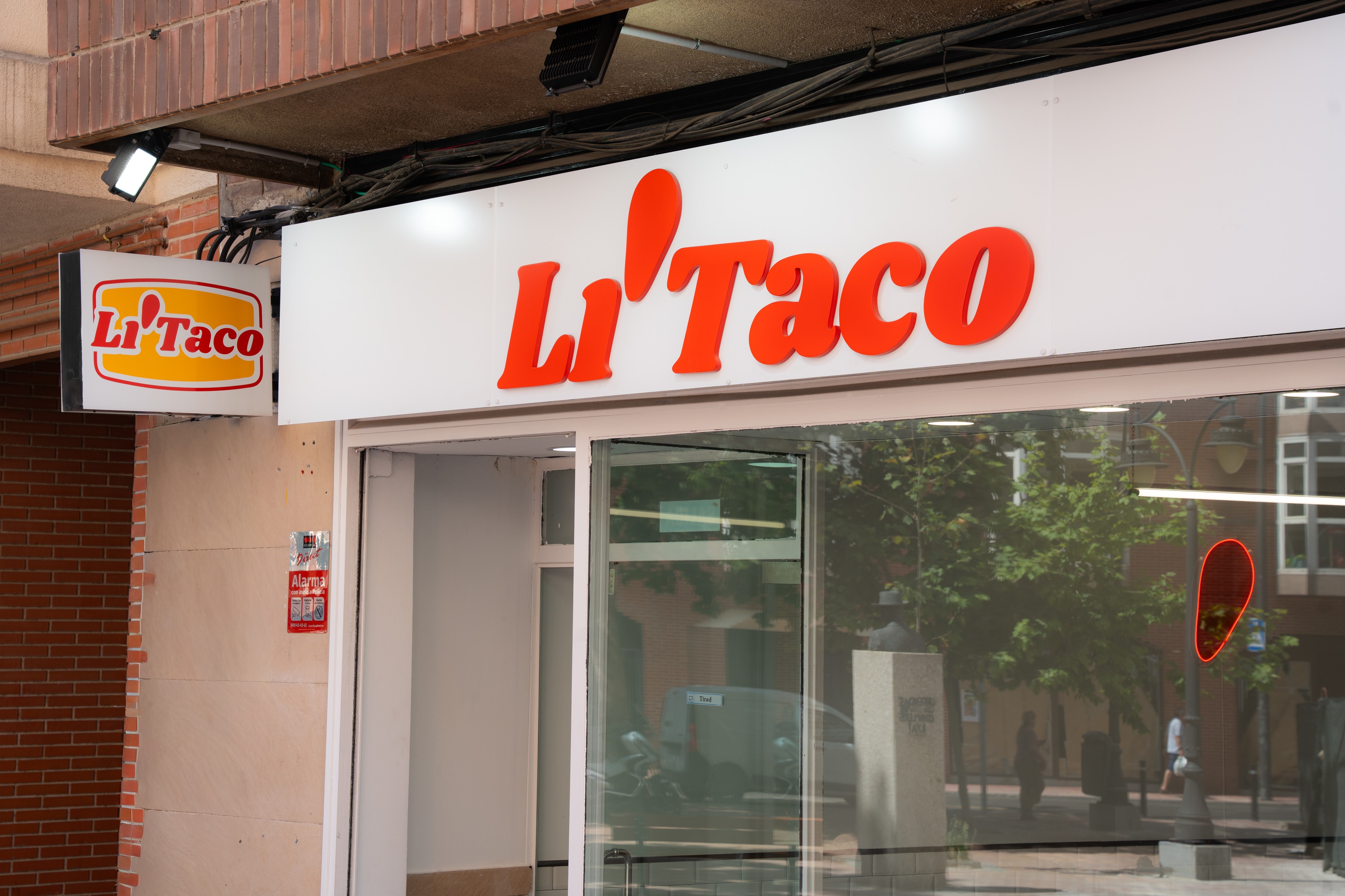 La fachada de Li'Taco en la calle San Eugenio: rótulo rojo sobre blanco, la caja de luz con el logo y la puerta abierta
