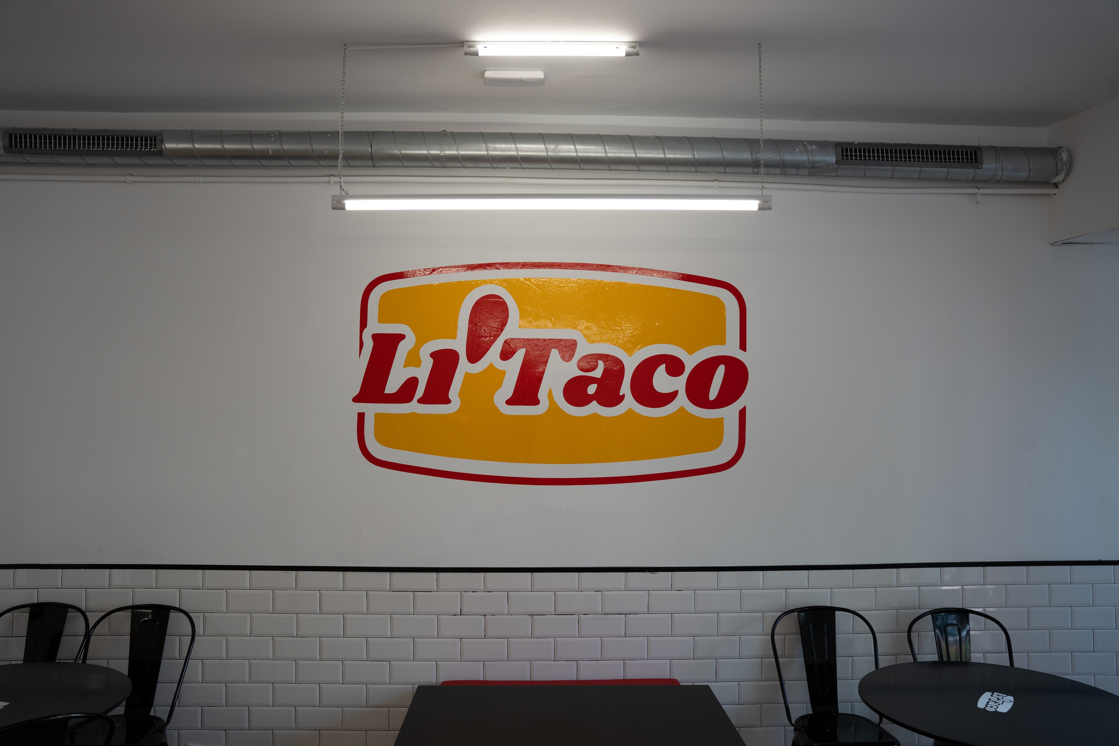 La sala de Li'Taco: el logo amarillo y rojo en la pared, azulejo blanco y mesas redondas