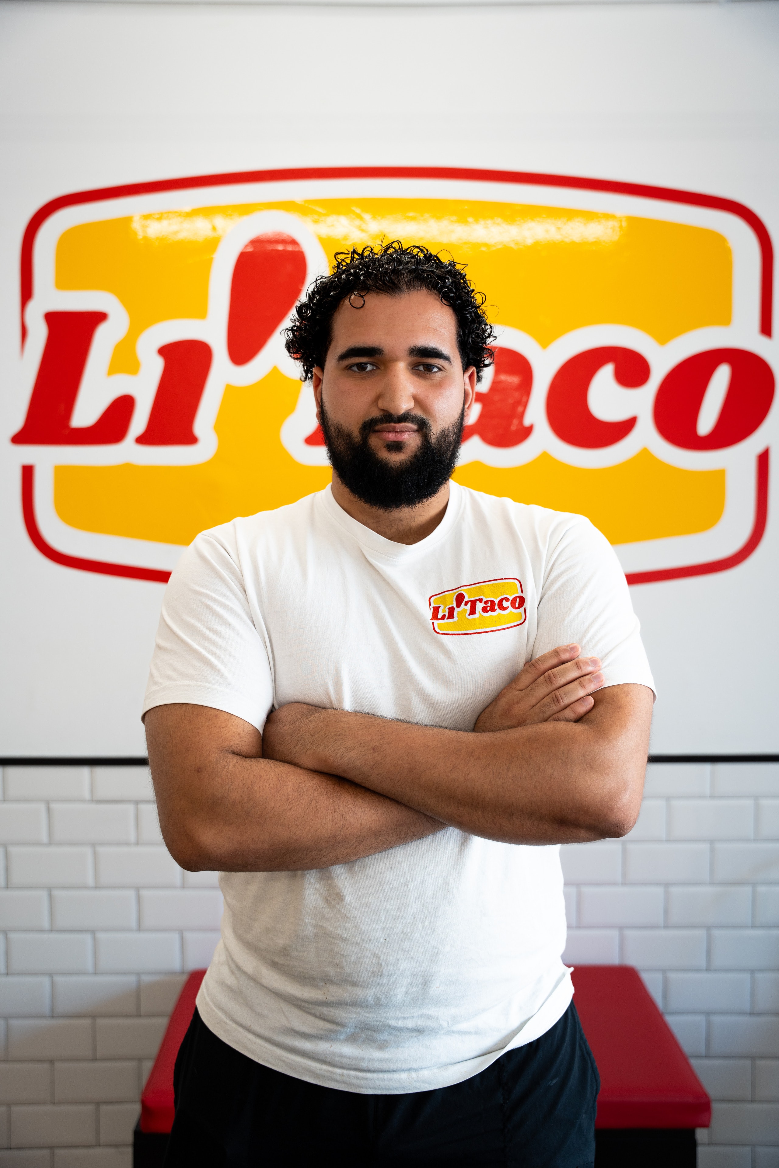 Un chico de Li'Taco, de brazos cruzados, delante del logo de la pared