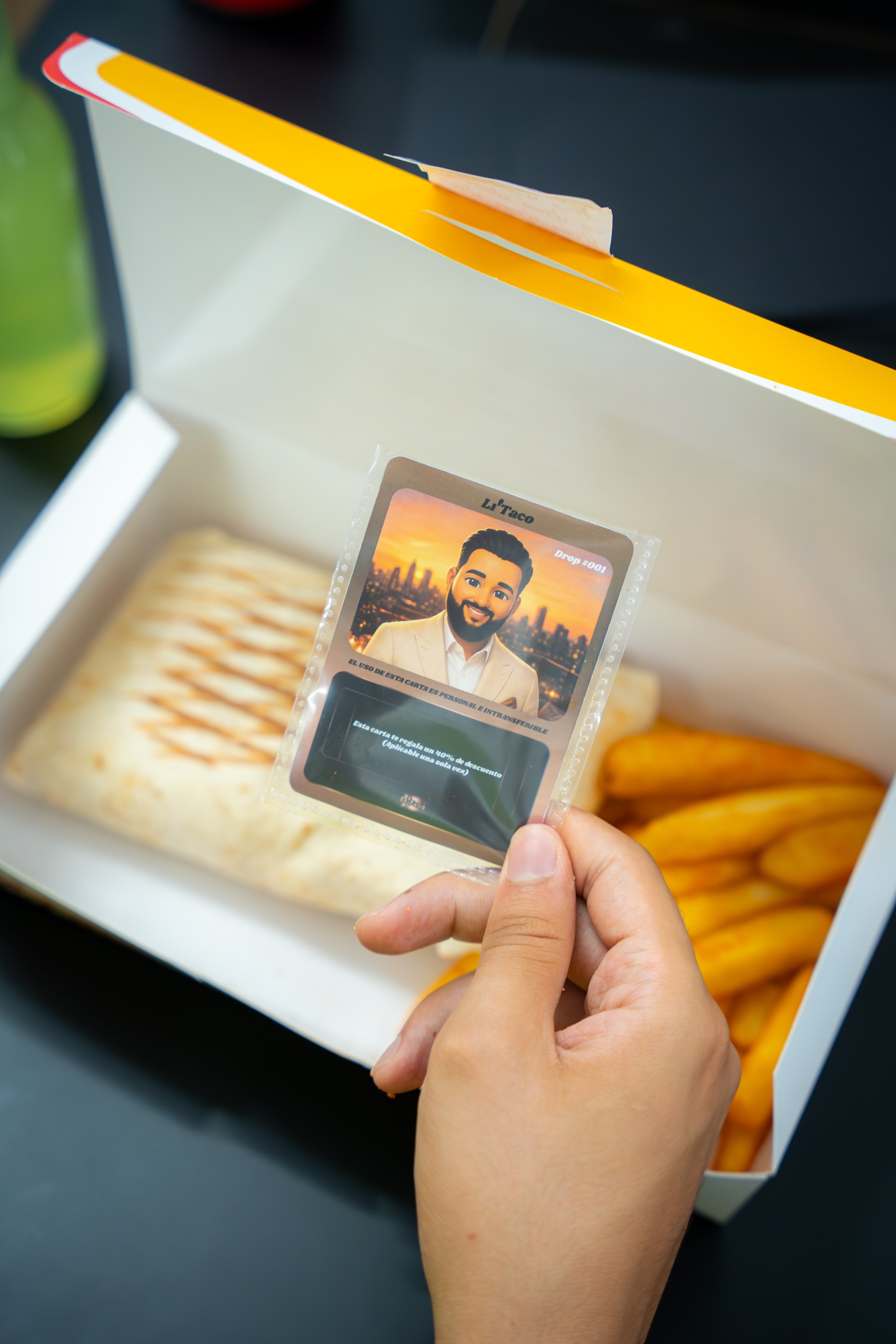 Una mano sostiene el cromo de bronce, el del 40% de descuento, sobre una caja abierta con taco y patatas